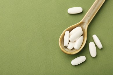 Photo of Vitamin pills in spoon on olive background, top view. Space for text