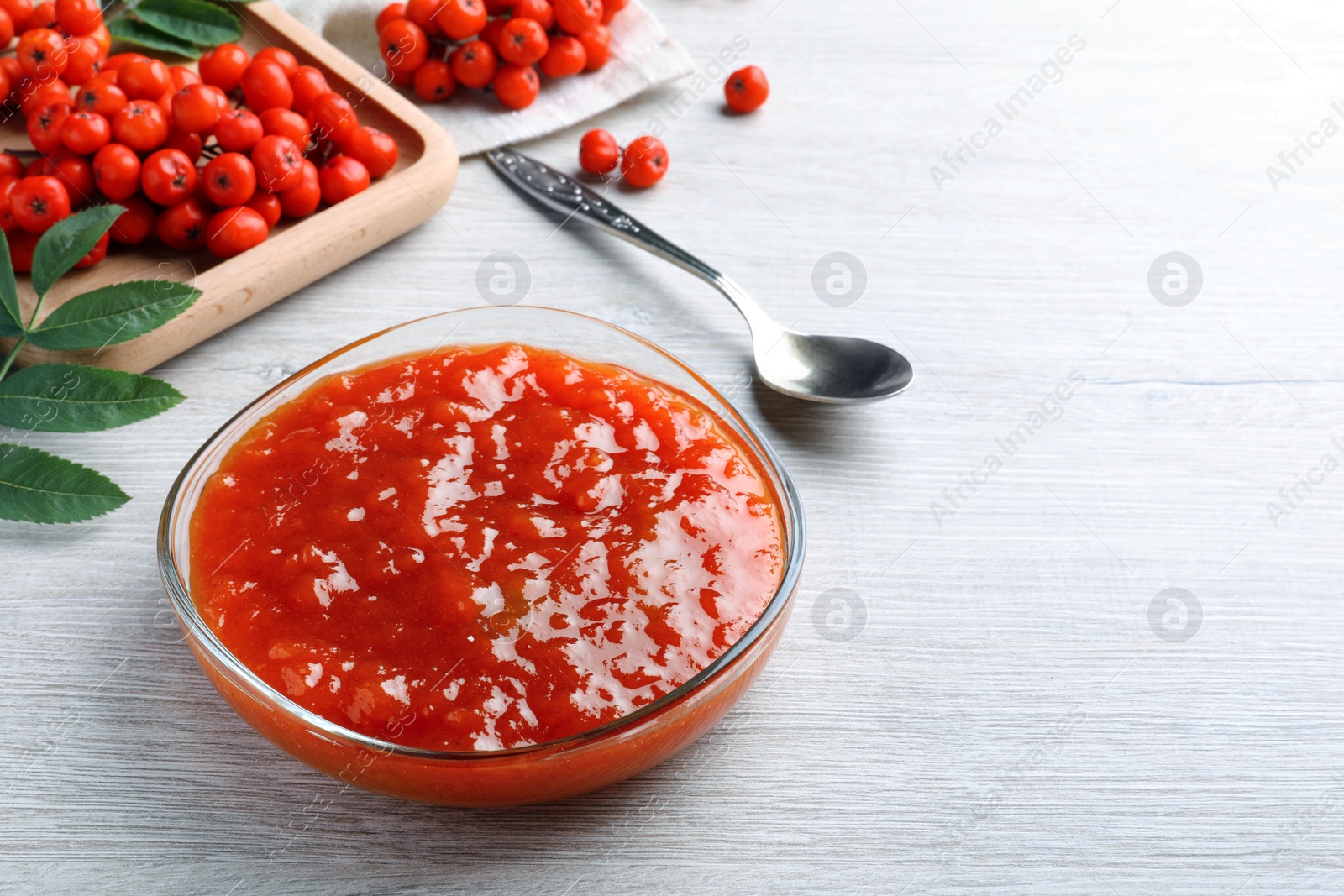 Photo of Delicious rowan jam in bowl on white wooden table. Space for text