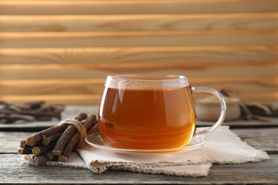 Photo of Aromatic licorice tea in cup and dried sticks of licorice root on wooden table