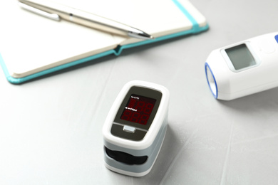 Photo of Modern fingertip pulse oximeter on light grey stone table, closeup