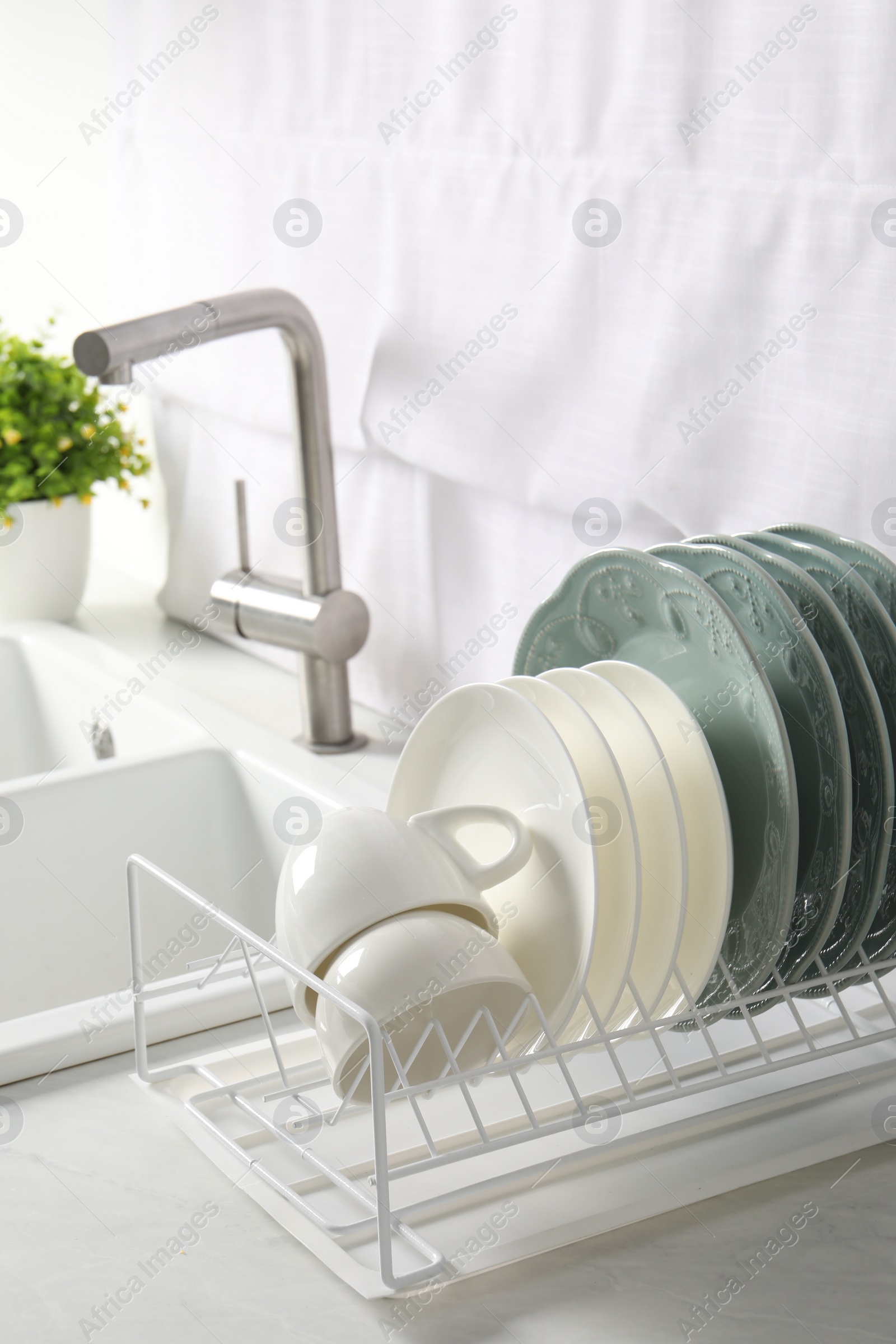 Photo of Drainer with different clean dishware and cups on white table in kitchen