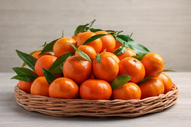 Fresh ripe juicy tangerines and green leaves on white wooden table