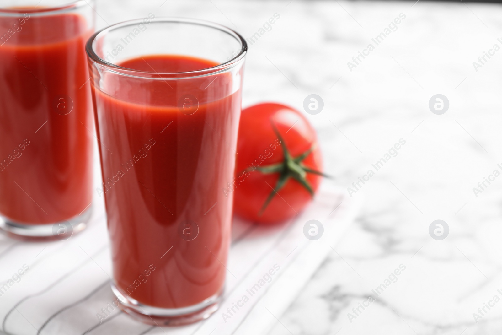 Photo of Delicious fresh tomato juice on white marble table, closeup. Space for text