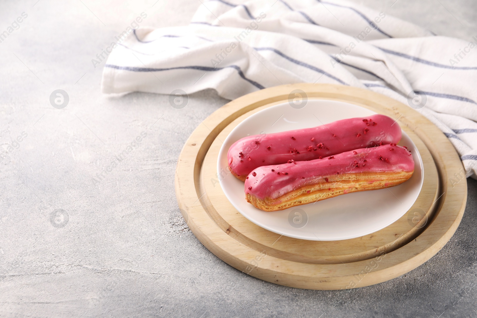 Photo of Plate with tasty glazed eclairs on grey textured table, closeup. Space for text