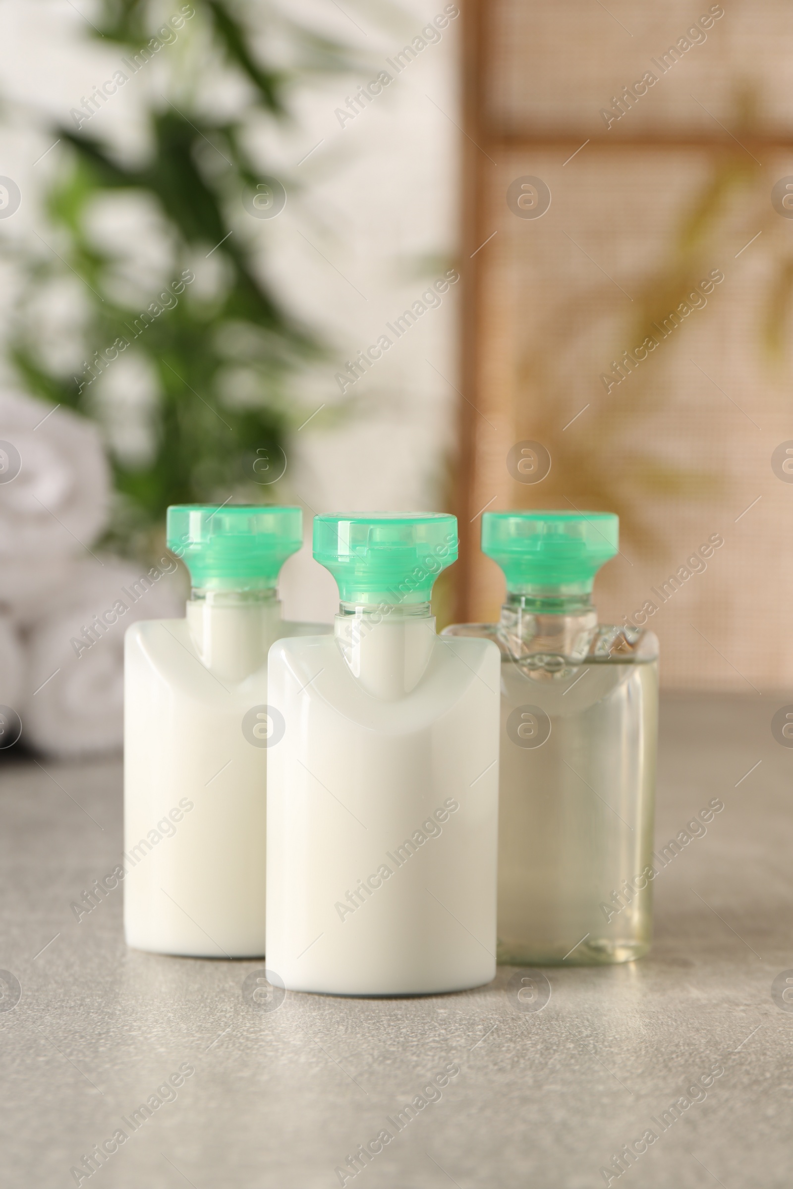 Photo of Mini bottles of cosmetic products on light grey table against blurred background