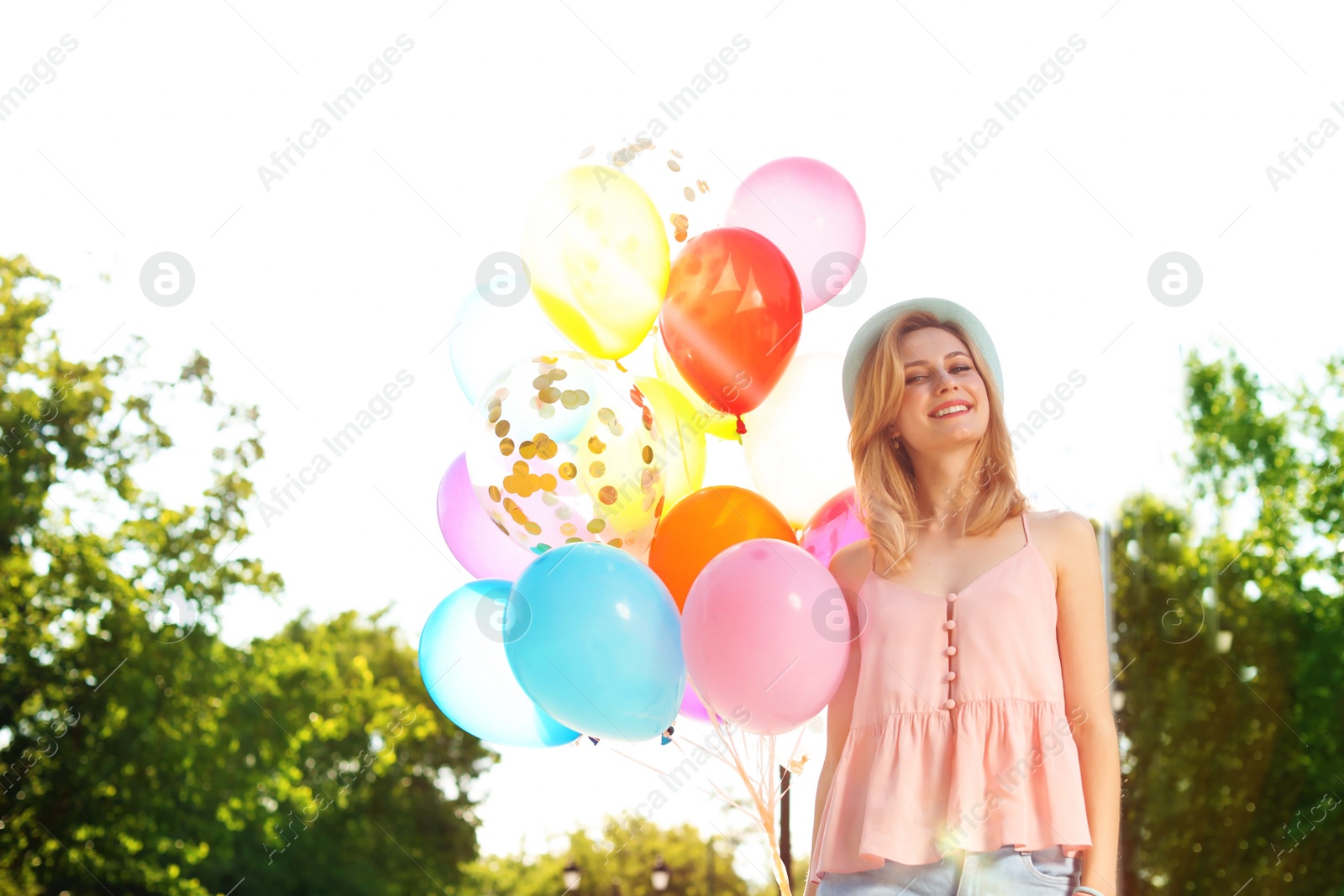 Photo of Young woman with colorful balloons outdoors on sunny day