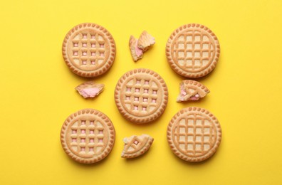 Tasty sandwich cookies with cream on yellow background, flat lay