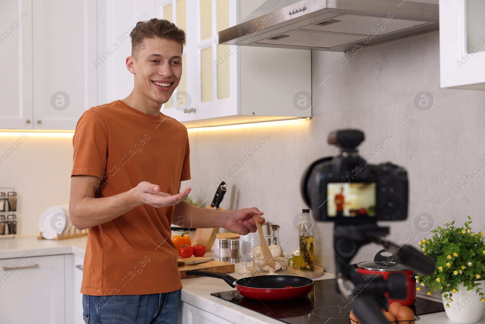 Photo of Smiling food blogger explaining something while recording video in kitchen