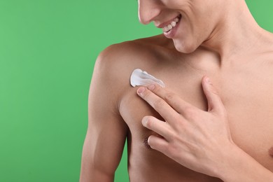 Photo of Man applying moisturizing cream onto his shoulder on green background, closeup. Space for text