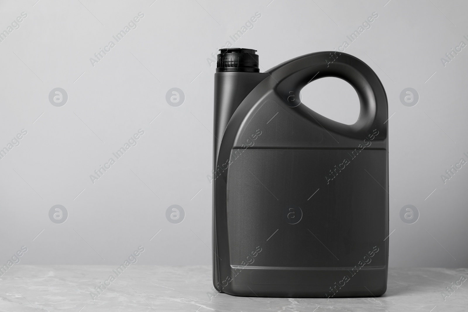Photo of Motor oil in grey canister on grey marble table against light background, space for text