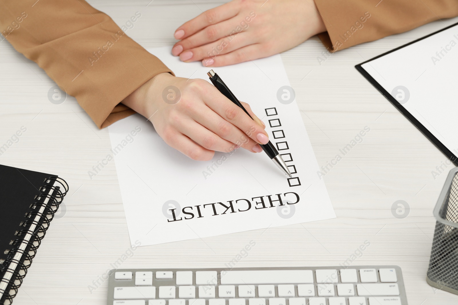 Photo of Woman filling Checklist at white wooden table, closeup