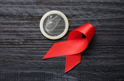 Photo of Red ribbon and condom on black wooden background, flat lay. AIDS disease awareness