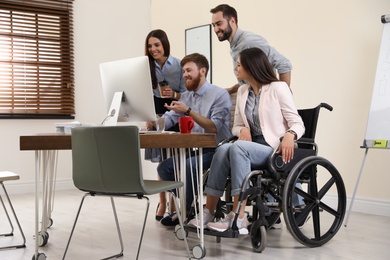 Photo of Young woman in wheelchair with colleagues at workplace