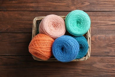 Colorful clews of threads in wicker basket on wooden table, top view