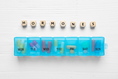 Photo of Word HORMONES made with wooden cubes and pill container on white table, flat lay