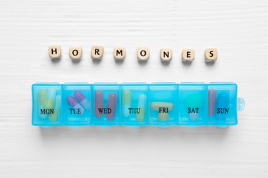 Word HORMONES made with wooden cubes and pill container on white table, flat lay