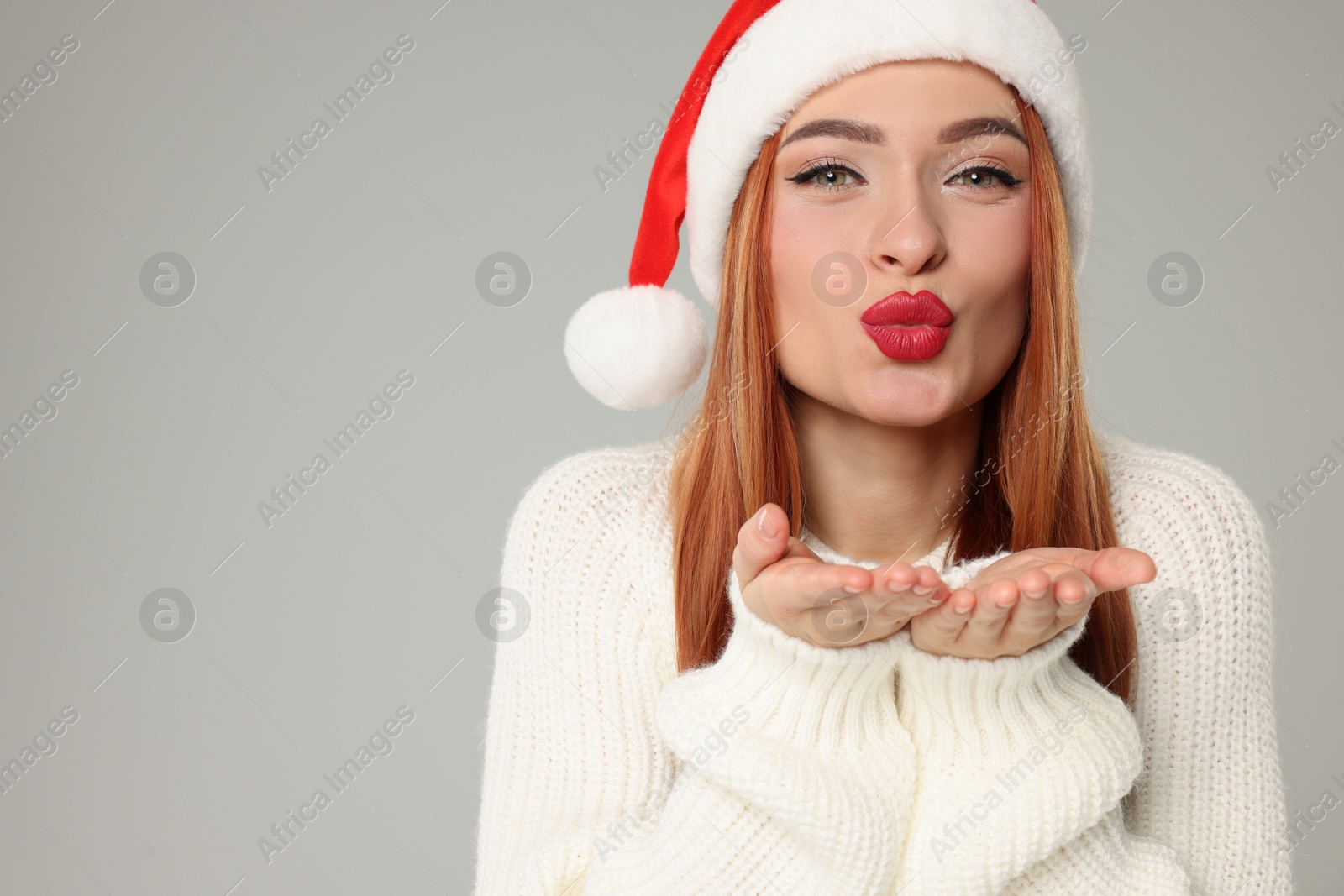 Photo of Young woman in Santa hat blowing kiss on light grey background, space for text. Christmas celebration