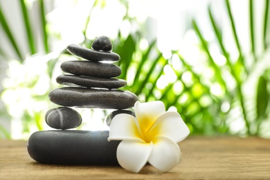 Photo of Table with stack of stones, flower and blurred green leaves on background, space for text. Zen concept