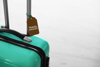 Photo of Stylish suitcase with travel insurance label on light background, closeup. Space for text