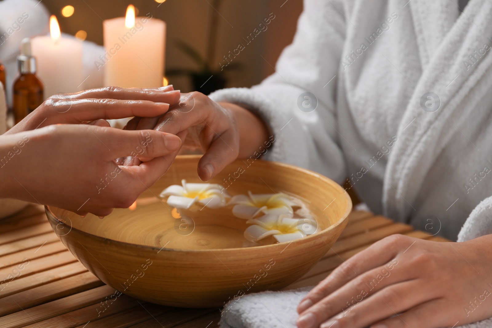 Photo of Woman receiving hand massage in spa salon, closeup. Bowl of water and flowers on wooden table