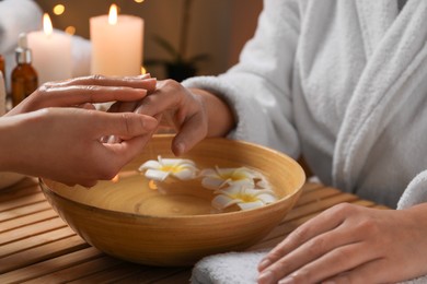 Woman receiving hand massage in spa salon, closeup. Bowl of water and flowers on wooden table