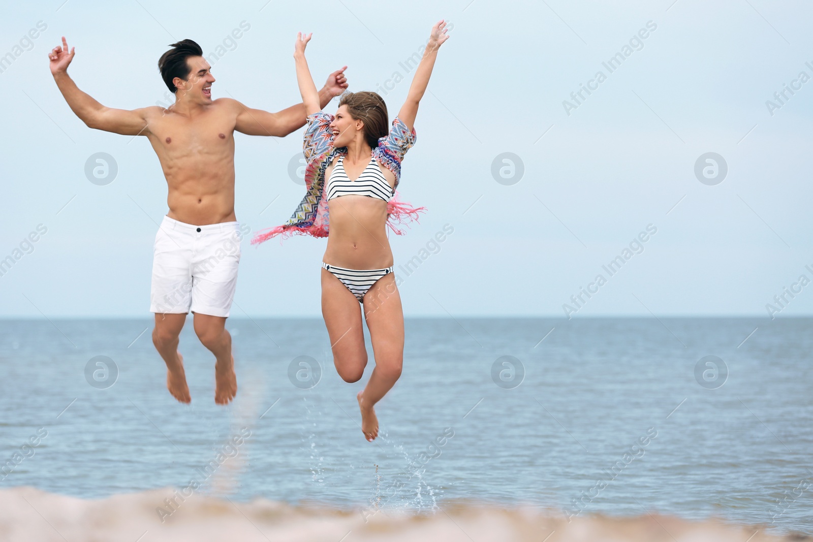 Photo of Happy young couple jumping together on sea beach. Space for text