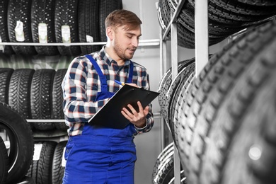 Photo of Young male mechanic with clipboard near tires in automobile service center