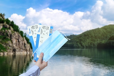 Image of Man holding tickets and protective mask outdoors, closeup. Travel during quarantine