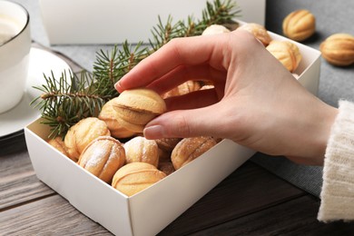 Photo of Woman taking delicious nut shaped cookies from box at wooden table, closeup