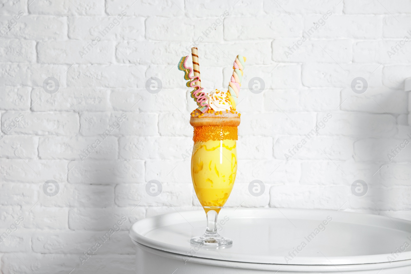 Photo of Glass of tasty milk shake with sweets on table near brick wall