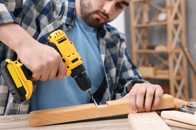 Photo of Young handyman working with electric drill at table in workshop, closeup