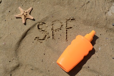 Photo of Abbreviation SPF written on sand, blank bottle of sunscreen and starfish at beach, flat lay