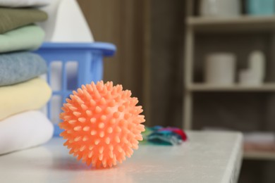 Orange dryer ball on white table near stacked clean towels in laundry room, closeup. Space for text