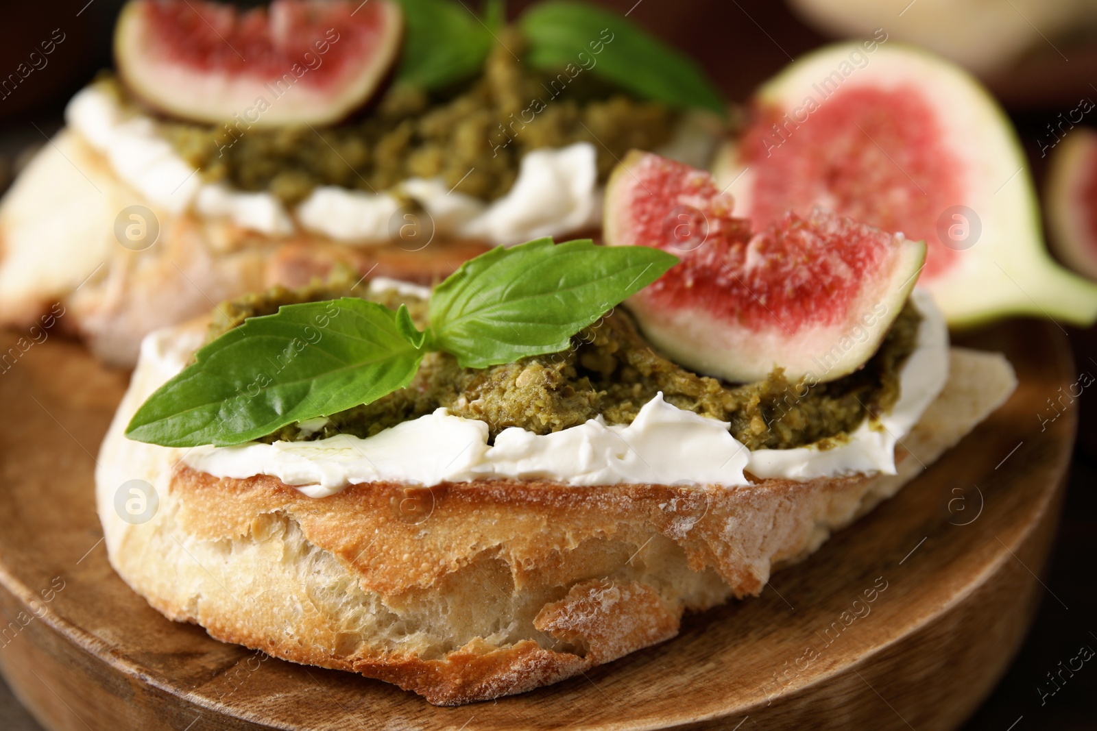 Photo of Tasty bruschettas with cream cheese, pesto sauce, figs and fresh basil on wooden board, closeup