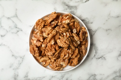 Plate with walnuts on marble background, top view