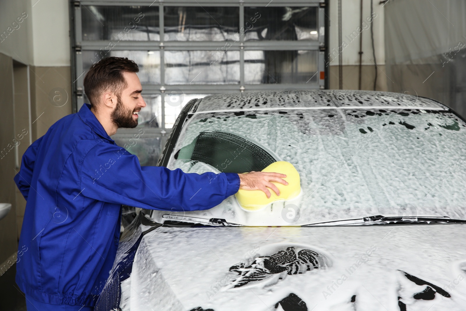 Photo of Worker cleaning automobile windshield with sponge at professional car wash