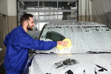 Worker cleaning automobile windshield with sponge at professional car wash