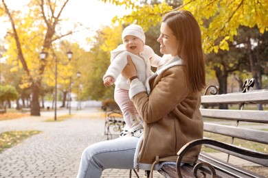 Photo of Happy mother with her baby daughter on bench in autumn park, space for text