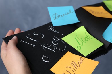 Woman holding notebook with written different baby names on grey background, closeup