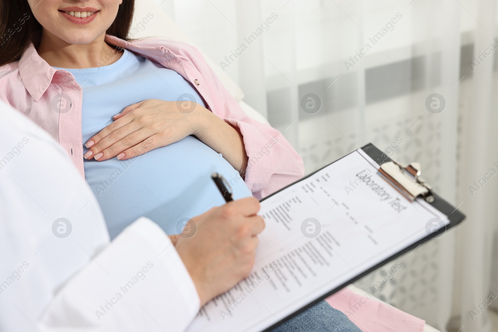 Photo of Doctor with results of laboratory test consulting smiling pregnant patient in clinic, closeup