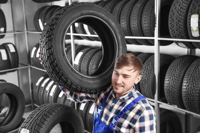 Photo of Young male mechanic with car tire in automobile service center