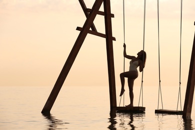 Photo of Young woman enjoying sunrise on swing over water