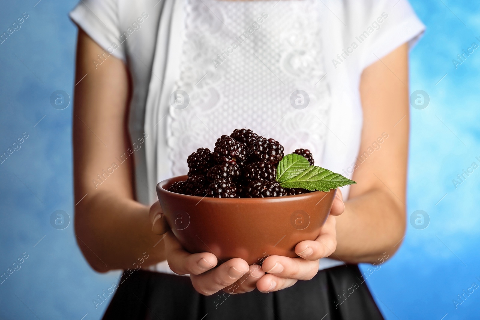 Photo of Woman holding bowl of fresh blackberry against color background, closeup