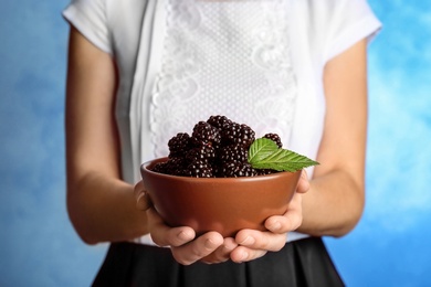 Photo of Woman holding bowl of fresh blackberry against color background, closeup