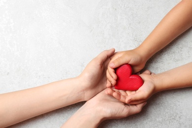 Woman and child holding heart on grey stone background, top view with space for text. Donation concept