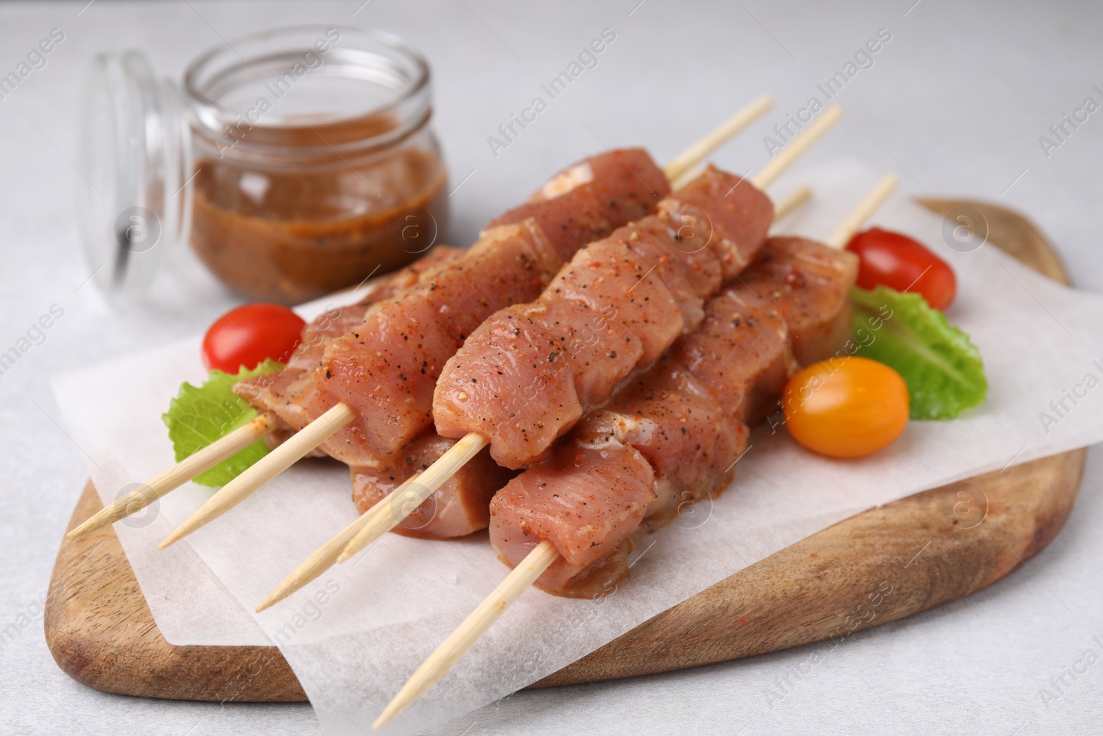 Photo of Wooden skewers with cut raw marinated meat on light grey table, closeup