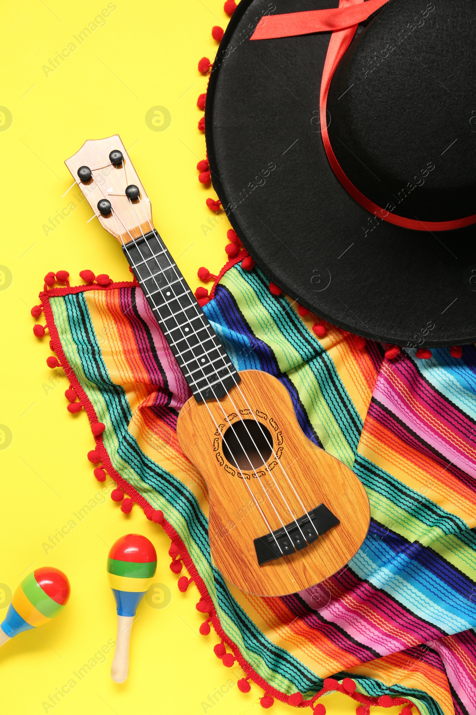 Photo of Mexican sombrero hat, guitar, maracas and colorful poncho on yellow background, flat lay