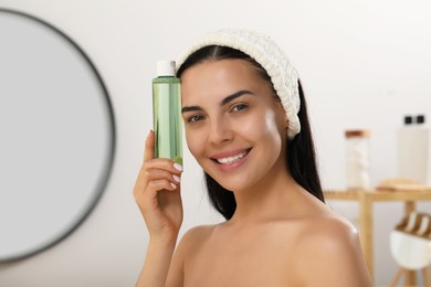 Photo of Young woman with bottle of micellar water indoors
