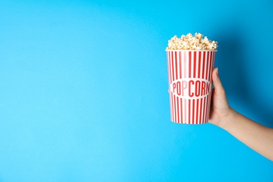 Photo of Woman holding popcorn cup on color background, closeup with space for text. Cinema snack