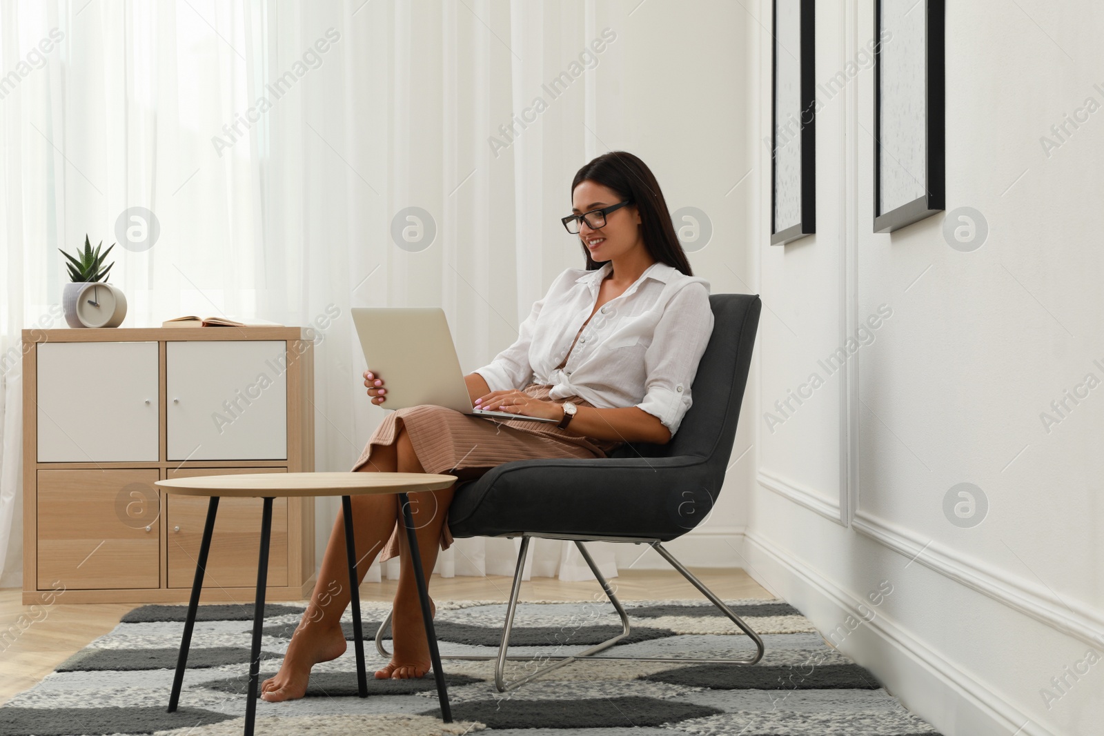 Photo of Young woman using laptop in armchair at home. Internet shopping